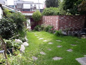 A well-maintained garden with stepping stones, a brick wall, and various plants. - Hans House (Seoul)