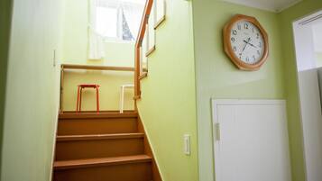 A staircase with wooden steps leading to a landing, a wooden-framed clock on the wall, and a white door to the right.