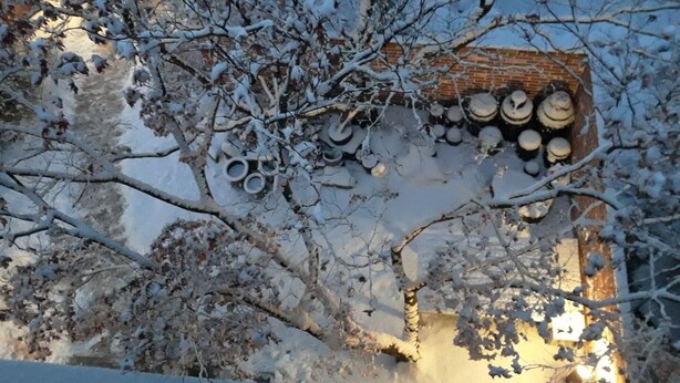 A snow-covered roof with a stack of cylindrical objects, possibly barrels, and a brick wall in the background. - Hans House (Seoul)