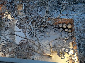 Ein mit Schnee bedecktes Dach, ein Stapel zylindrischer Objekte, vermutlich Fässer, und eine Ziegelwand im Hintergrund.
