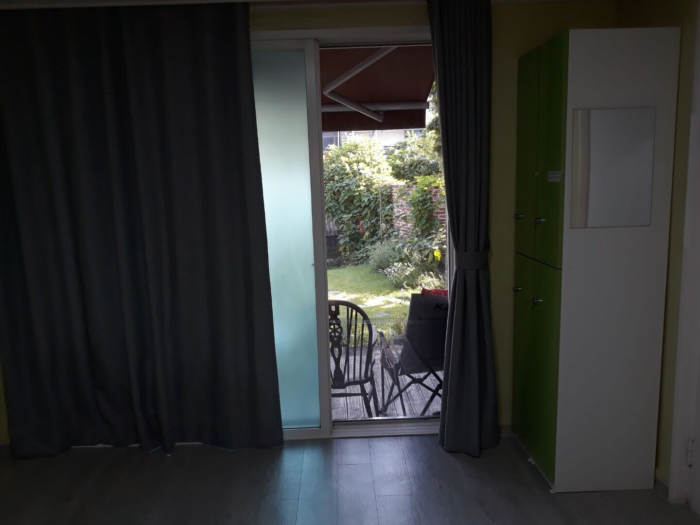 Ein Zimmer mit einer Schiebeglastür, die auf einen Balkon mit Stuhl und kleinem Tisch führt.