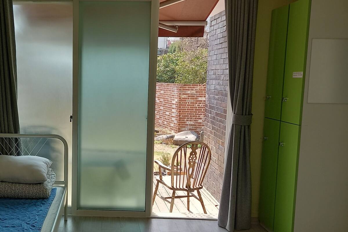 Una piccola stanza con un letto, una sedia e una porta scorrevole in vetro che dà su uno spazio all'aperto.