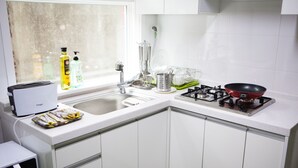 A kitchen with white cabinets, a gas stove, a toaster, and dish drying racks. - Hans House (Seoul)