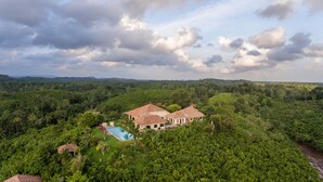 A large house with a swimming pool surrounded by lush greenery and hills in the background.