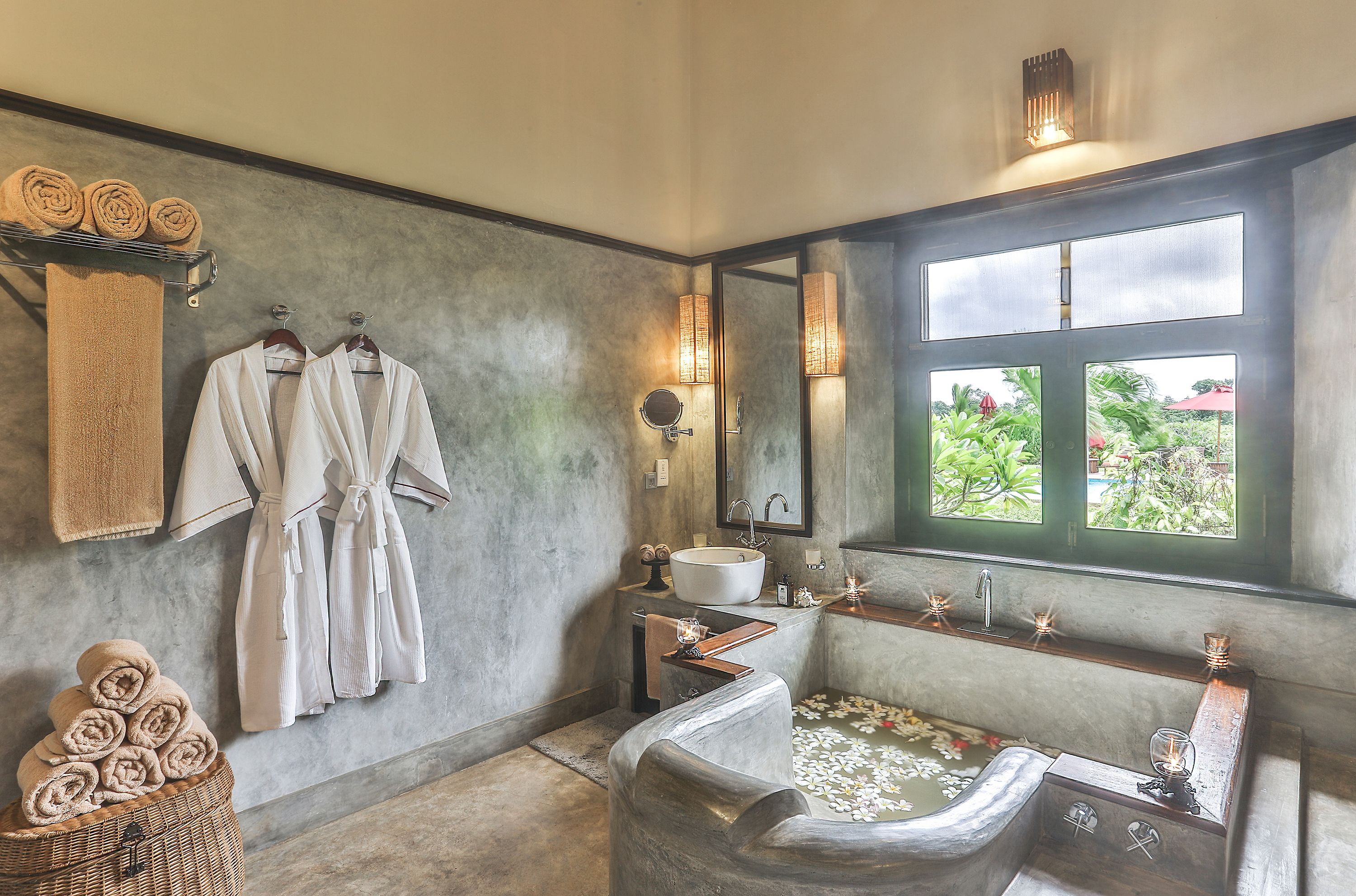 A bathroom with a large bathtub, a sink, and a window with a view of greenery.