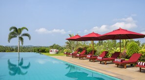 A poolside area with lounge chairs and red umbrellas, surrounded by lush greenery and a clear sky. - Villa Mayurana By Edwards Collection (Ahangama)