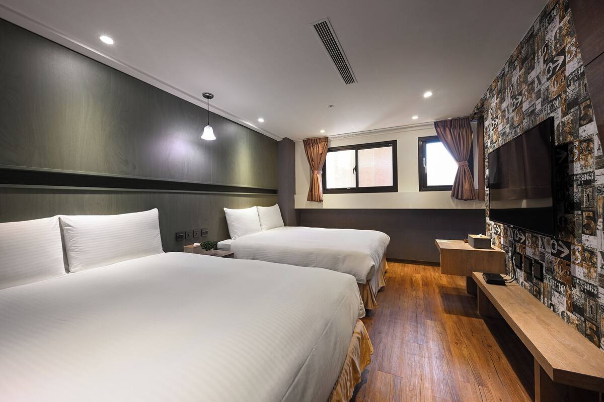 Une chambre d’hôtel avec deux lits, un plancher en bois, une télévision et un mur orné d’un collage d’images.