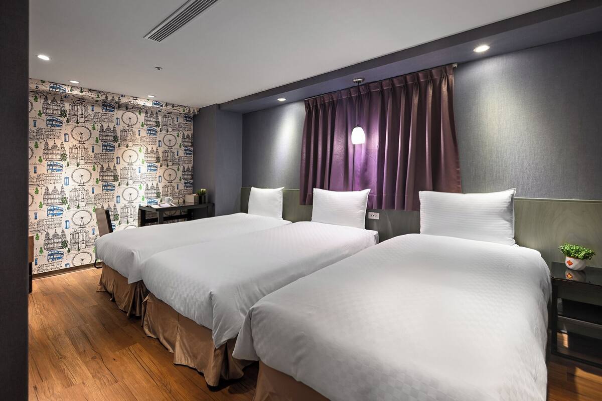 Une chambre d’hôtel avec deux lits, un mur de couleur sombre, un papier peint à motifs et une fenêtre ornée de rideaux violets.
