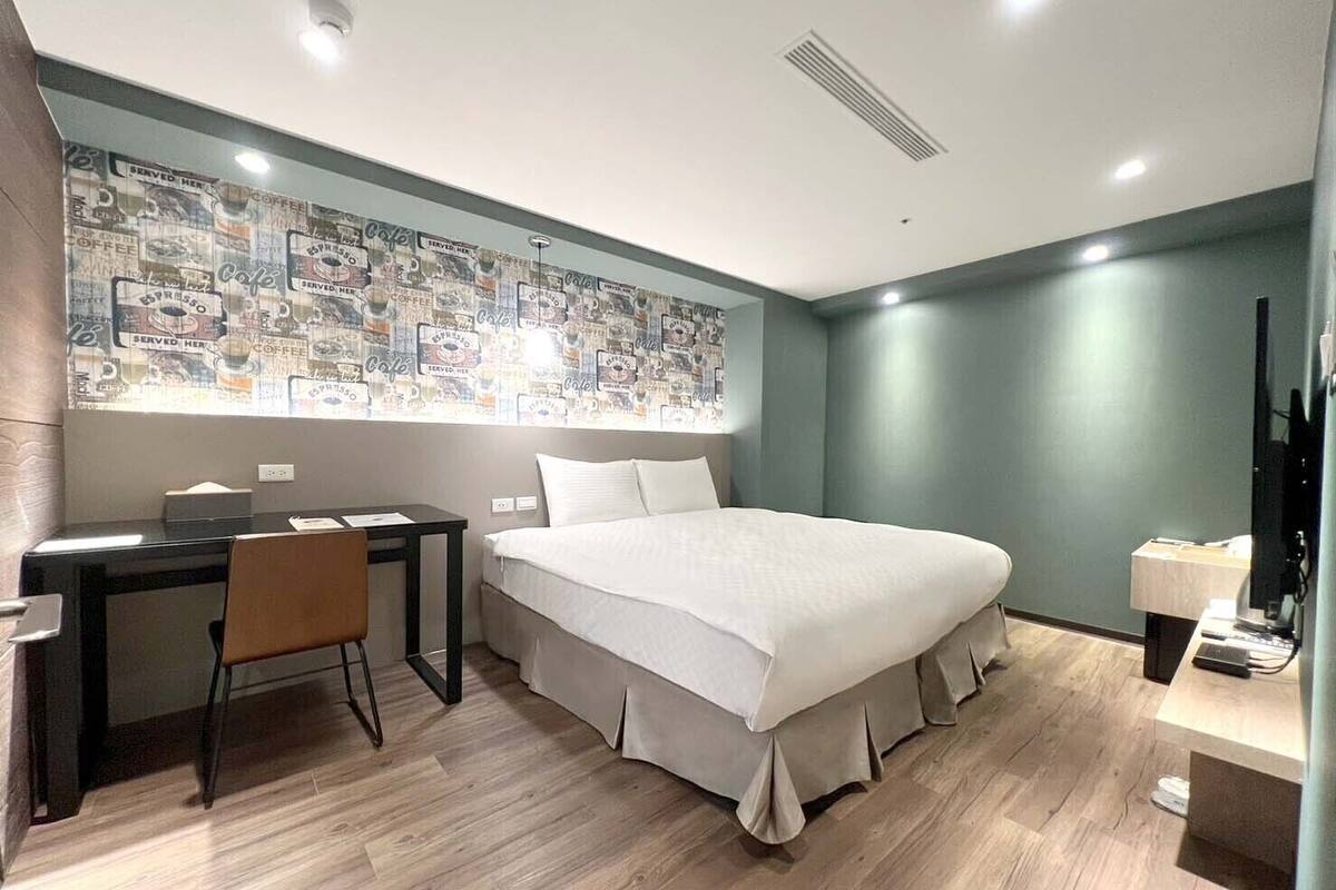 Une chambre d’hôtel moderne dotée d’un grand lit, d’un bureau avec une chaise et d’un mur décoré d’un papier peint sur le thème du café.