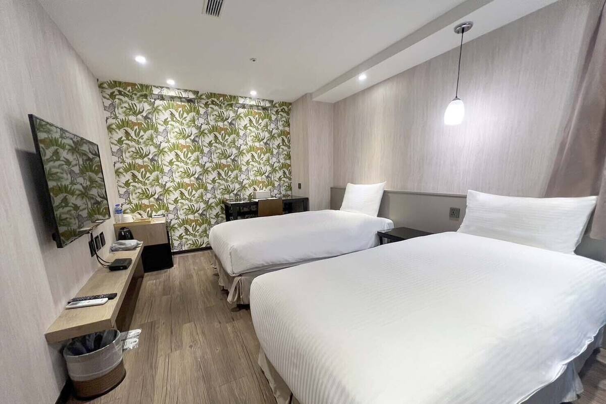 Une chambre d’hôtel avec deux lits, une télévision, un bureau et une poubelle.