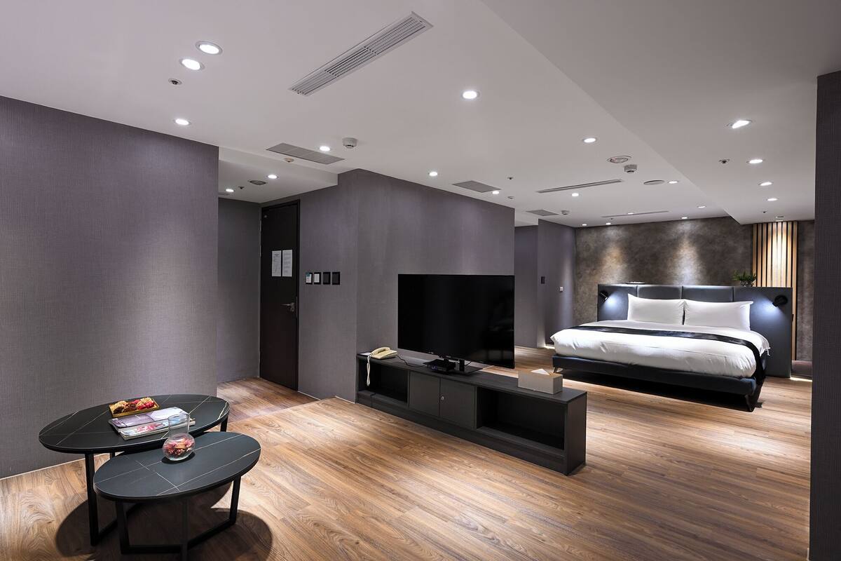 Une chambre moderne avec un grand lit, une télévision et un petit coin salon comprenant une table et des chaises.