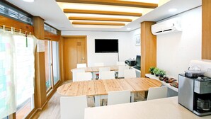Un salón de conferencias con una mesa de madera, sillas blancas, un televisor de pantalla plana y un equipo de aire acondicionado.