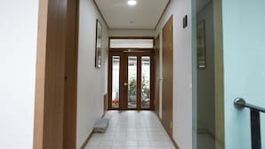 Un pasillo con puertas de madera, piso de baldosas y un pequeño banco.