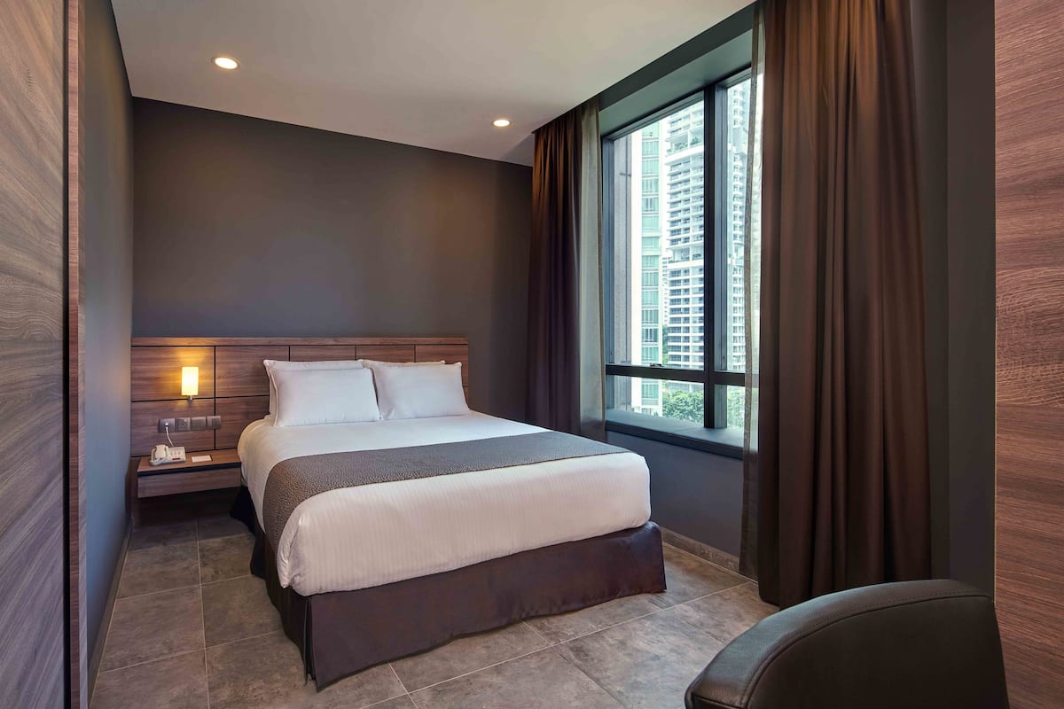 Ein modernes Hotelzimmer mit einem großen Bett, einem Nachttisch, einer Wandleuchte und einem mit Vorhängen versehenen Fenster.