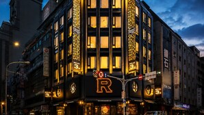 Um hotel com um letreiro grande em formato de 'R', várias varandas e sinalização iluminada.