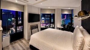 Quarto de hotel moderno com uma cama grande, televisão de tela plana e vista para a cidade pelas janelas.