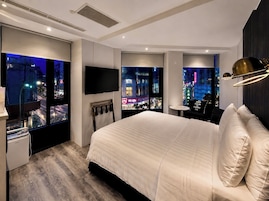 Een moderne hotelkamer met een groot bed, een flatscreen televisie en uitzicht op de stad door de ramen.
