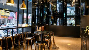 Uma área de bar moderna, com banquetas altas, iluminação pendente e vista para a rua.