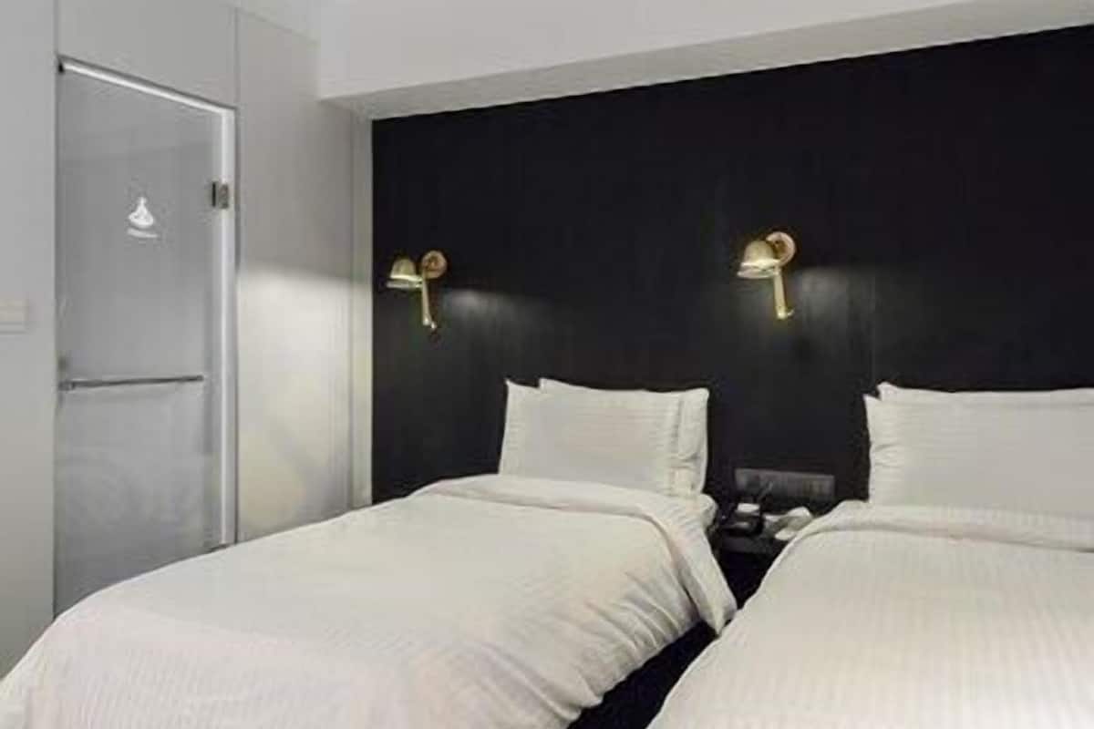 Une chambre d’hôtel avec deux lits, une tête de lit sombre et une porte.