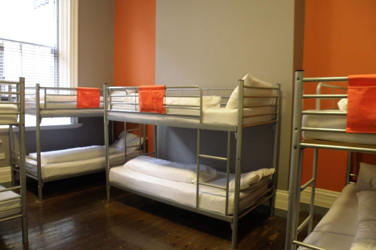 A room with bunk beds, wooden flooring, and orange walls.