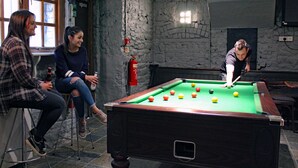 A pool table in a room with stone walls, a fire extinguisher, and a television mounted on the wall. - Albatross Hostel (Newcastle-upon-Tyne)