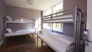 A room with two bunk beds, wooden flooring, and large windows allowing natural light. - Albatross Hostel (Newcastle-upon-Tyne)
