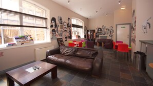 A spacious lobby with a leather sofa, a wooden coffee table, and a variety of colorful chairs. - Albatross Hostel (Newcastle-upon-Tyne)
