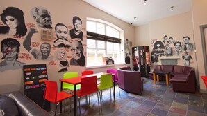 A room with colorful chairs, a vending machine, and a wall with various portraits and quotes. - Albatross Hostel (Newcastle-upon-Tyne)