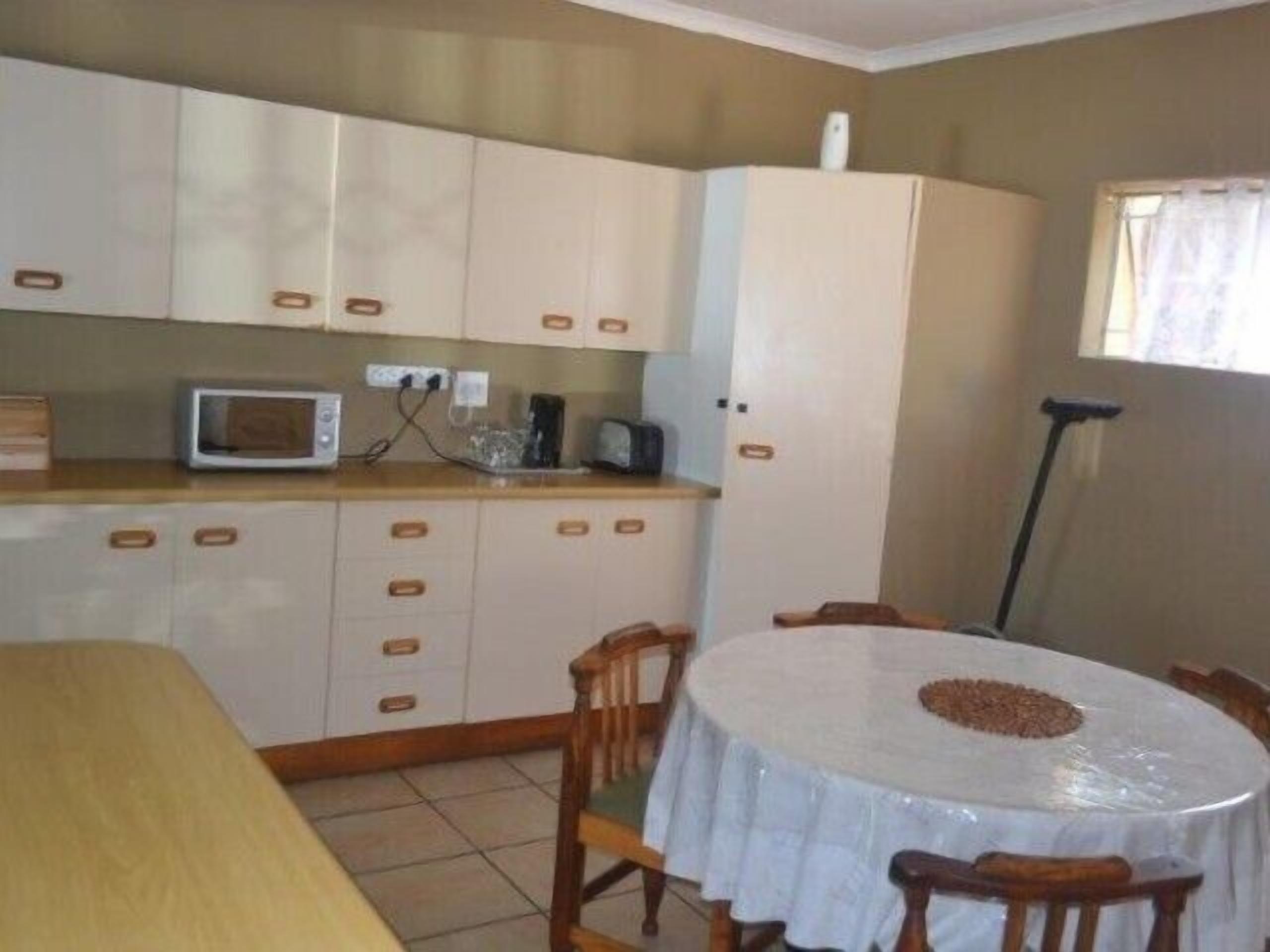 Una cocina compacta con microondas, tostadora y armarios. Hay una mesa de comedor con sillas y una ventana con cortinas.
