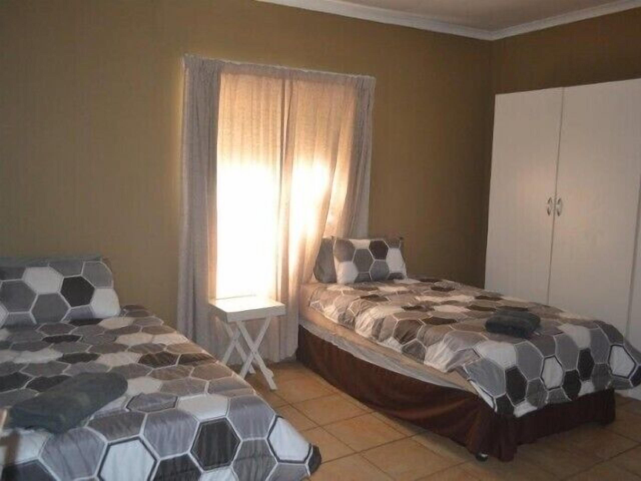 A bedroom with two beds, a window with curtains, a wardrobe, and a small table.