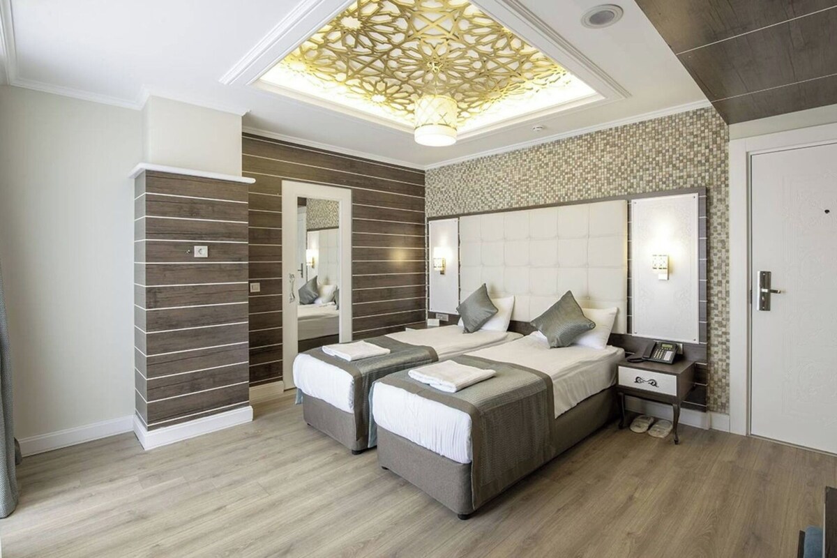 Quarto moderno com uma cama grande, duas mesas de cabeceira, um espelho e um lustre.