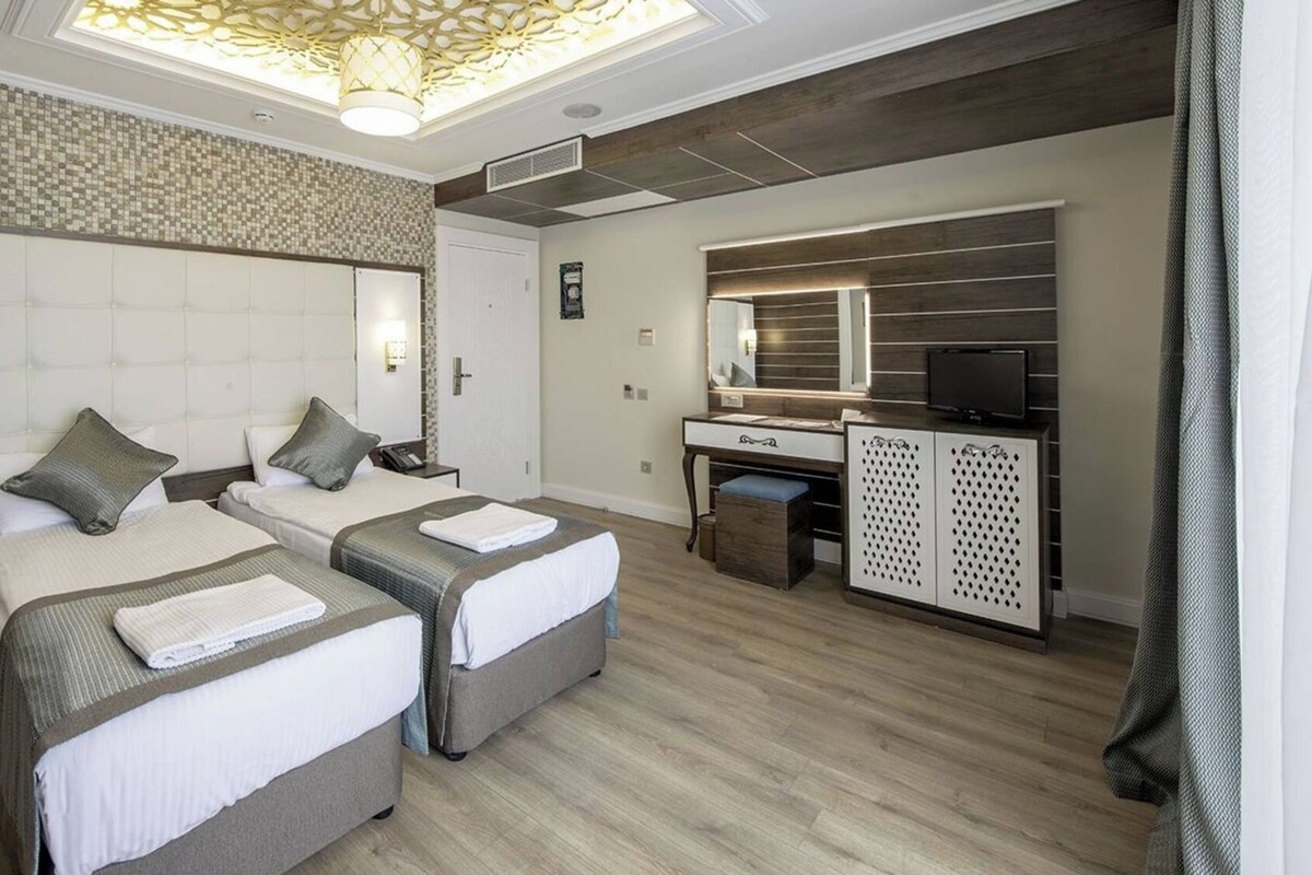 Habitación de hotel con dos camas, un escritorio, un espejo y un armario.