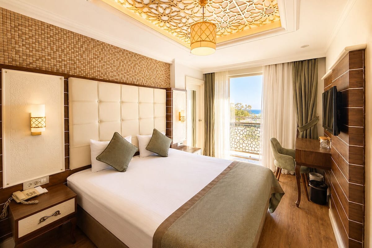 A hotel room with a large bed, a TV, a desk, and a balcony with a view.