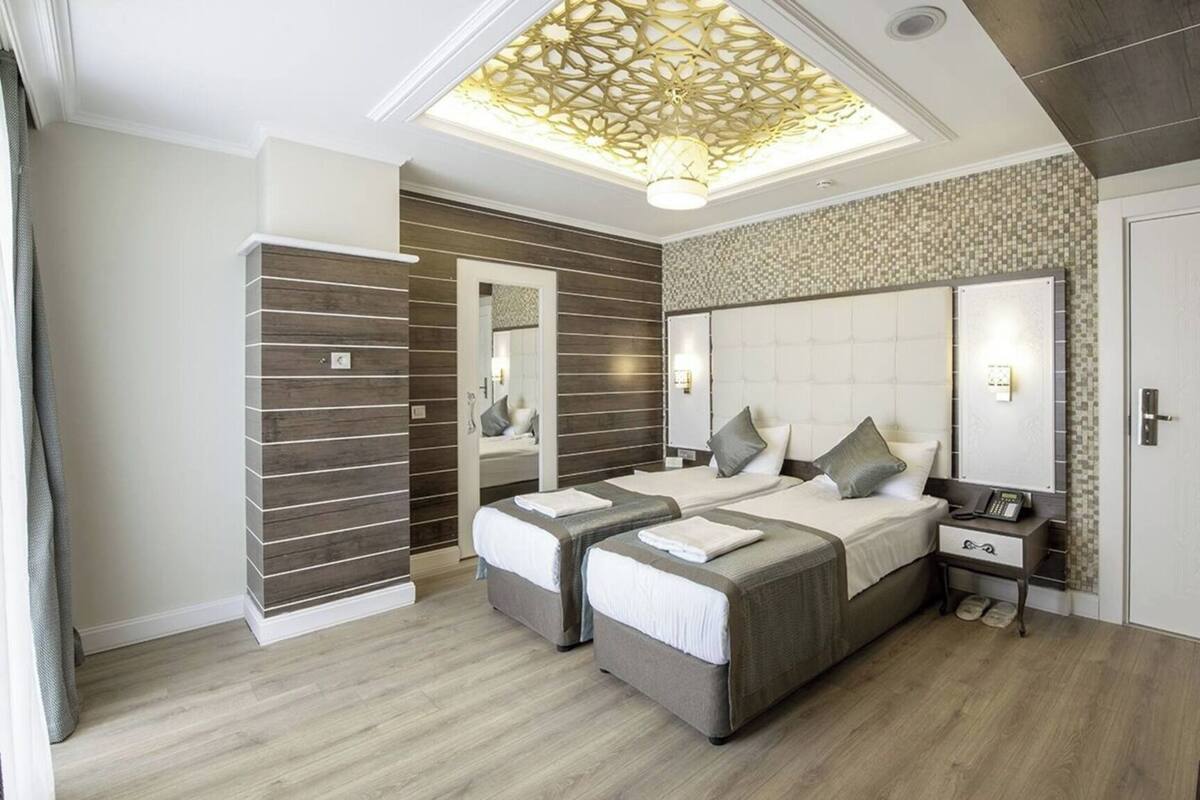 A modern bedroom with a large bed, two bedside tables, a mirror, and a ceiling light fixture.