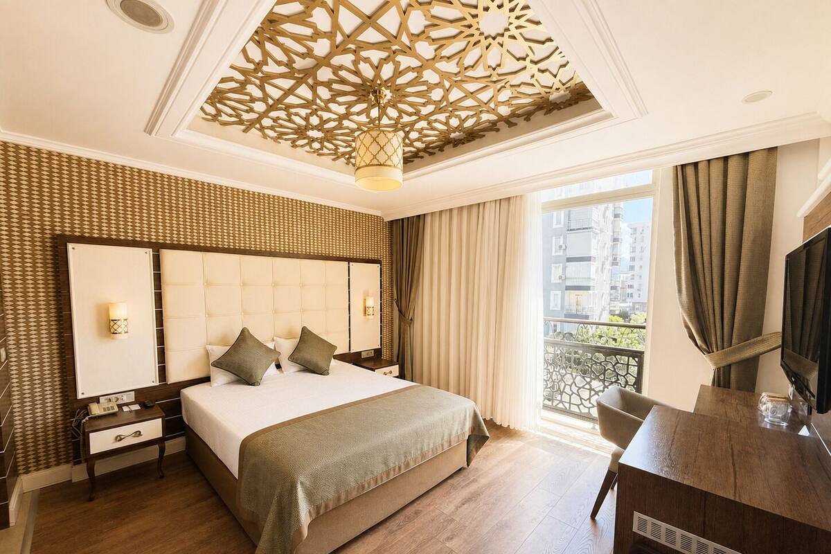 A hotel room with a large bed, a desk, a TV, a balcony with a view, and a decorative ceiling.