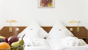 Habitación de hotel con dos camas, ropa de cama blanca, una cesta de frutas y un cuadro en la pared.