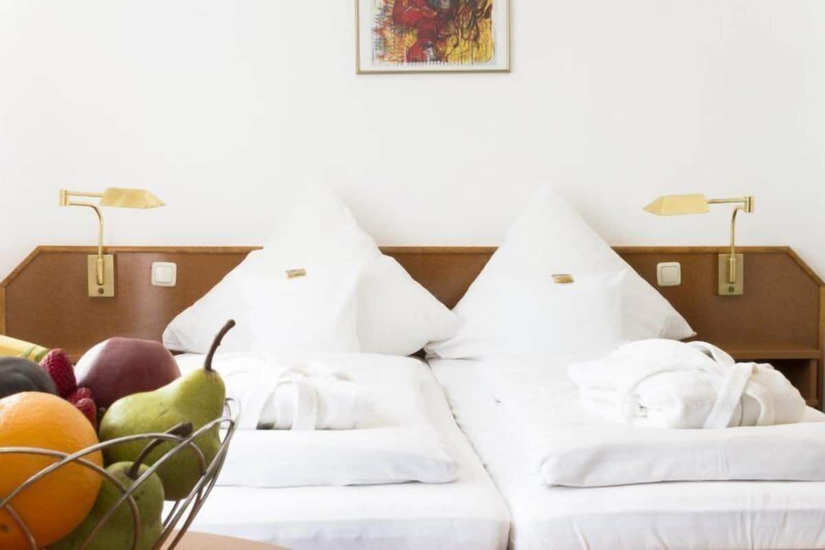 A hotel room with two beds, white bedding, a fruit basket, and a painting on the wall.