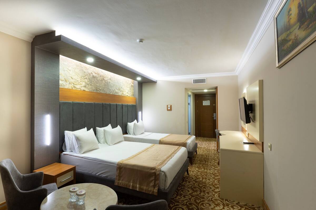 A hotel room with two beds, a small table, a chair, a TV, and a painting on the wall.
