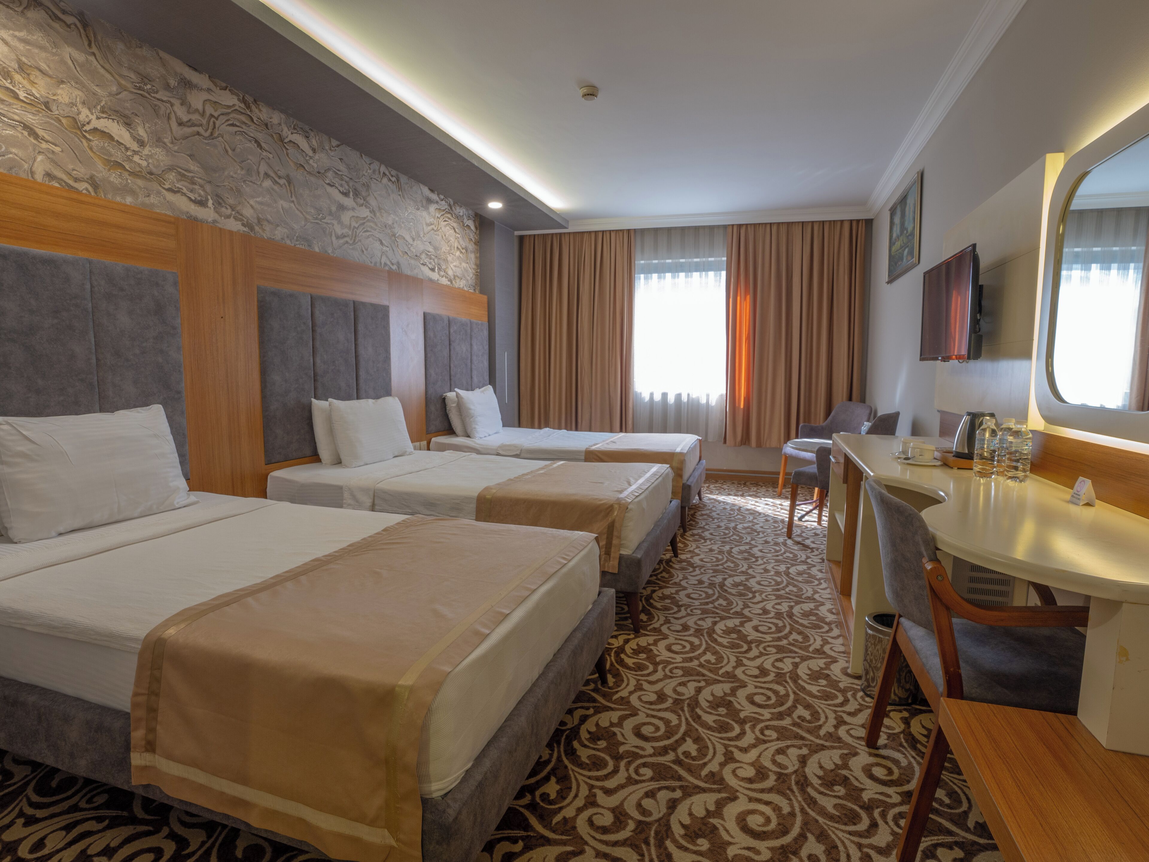 Habitación de hotel con tres camas, un escritorio, una silla y un espejo grande.