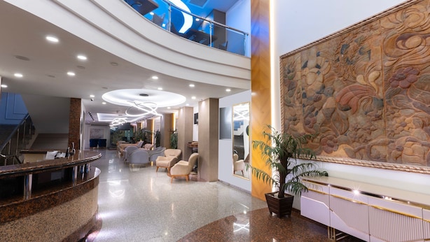 Un lobby espacioso con techo alto, un área de estar central, una recepción y un amplio mural decorativo.