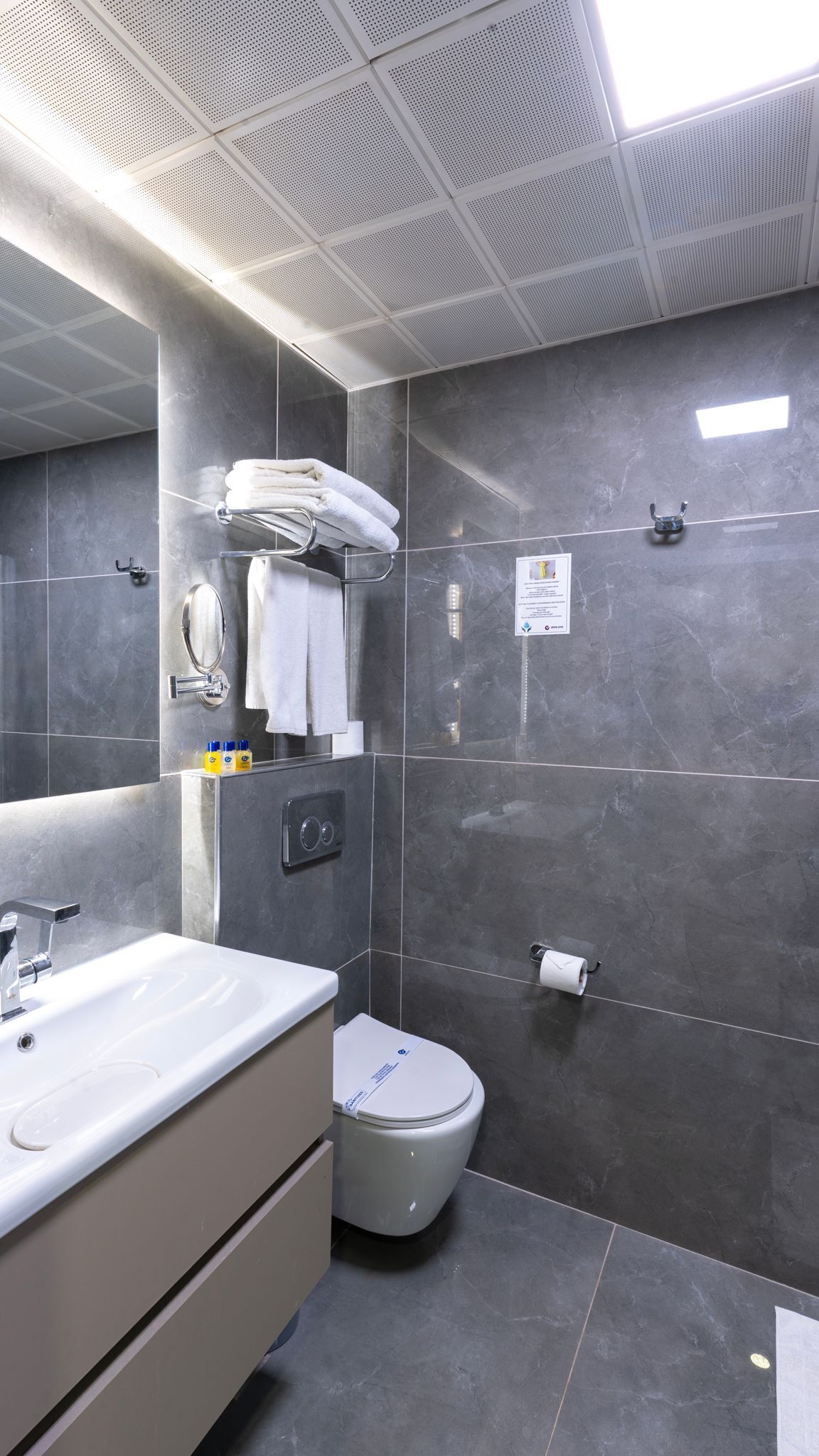 A modern bathroom with a large mirror, a white sink, a toilet, and a shower area.