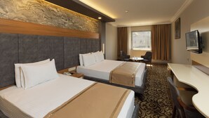 Habitación de hotel con dos camas, un escritorio, una silla, televisor y ventana con cortinas.
