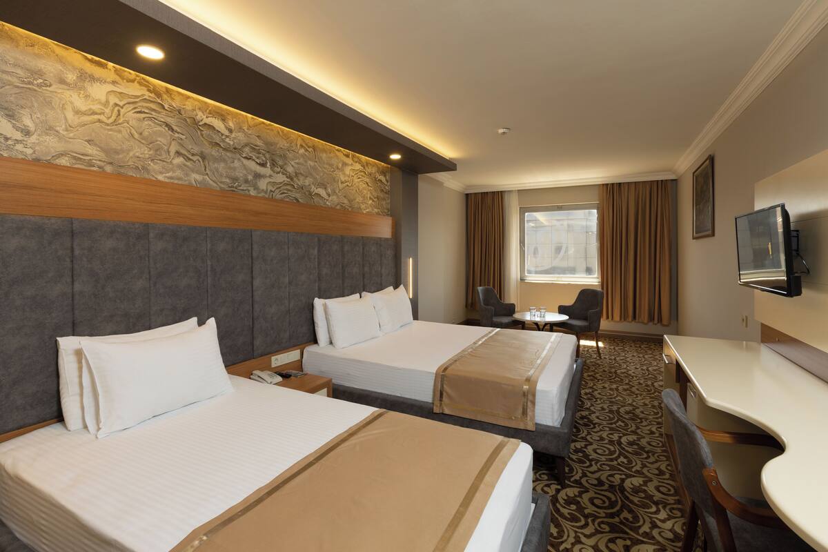 A hotel room with two beds, a desk, a chair, a television, and a window with curtains.