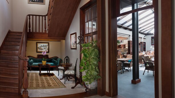 A spacious living area with a wooden staircase, a green sofa, a coffee table, and a large potted plant.