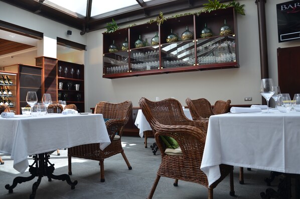 A dining area with wicker chairs and tables, a glass display case with bottles, and a bar sign.