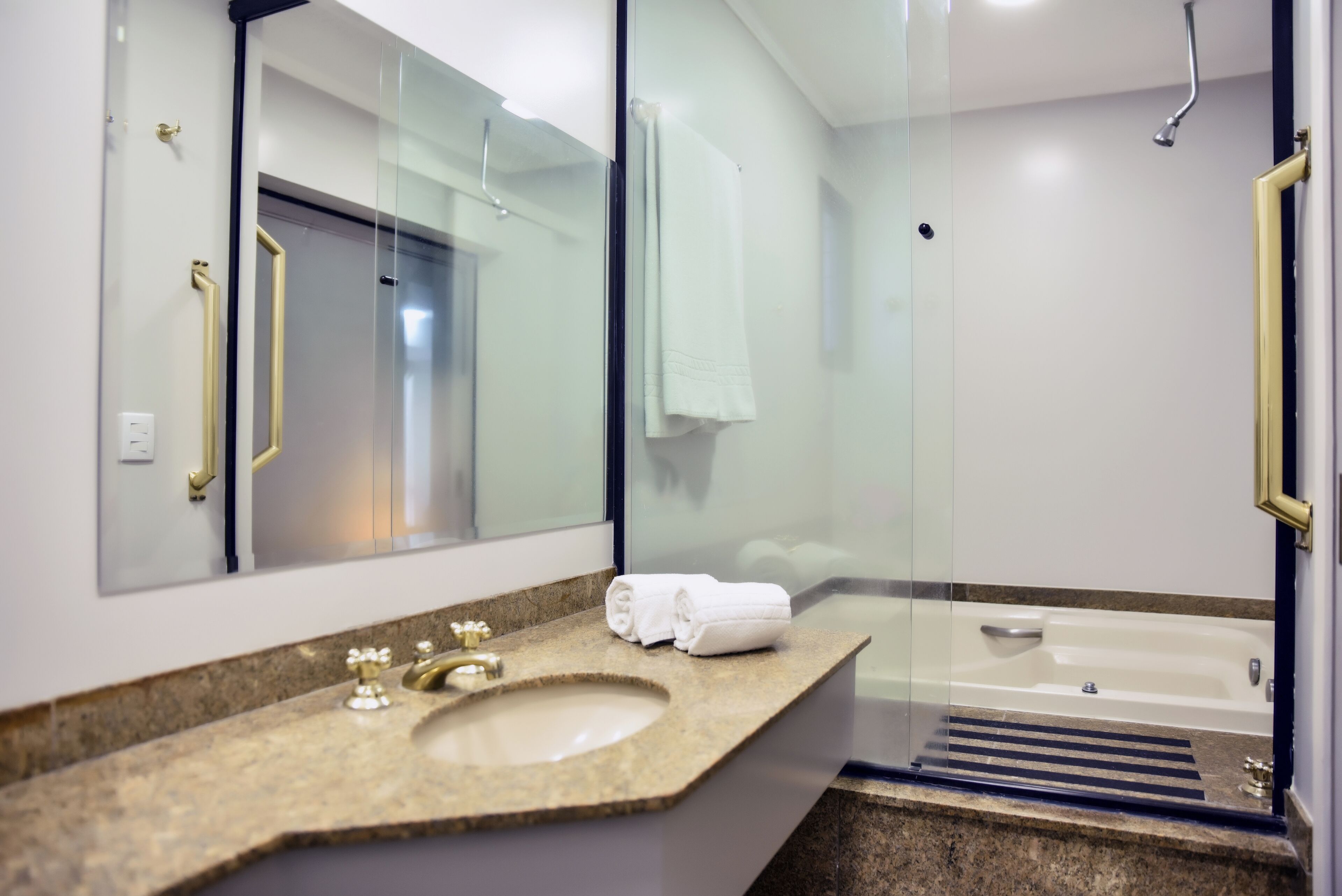 A modern bathroom with a granite countertop sink, a large mirror, a glass-enclosed shower, and a bathtub.
