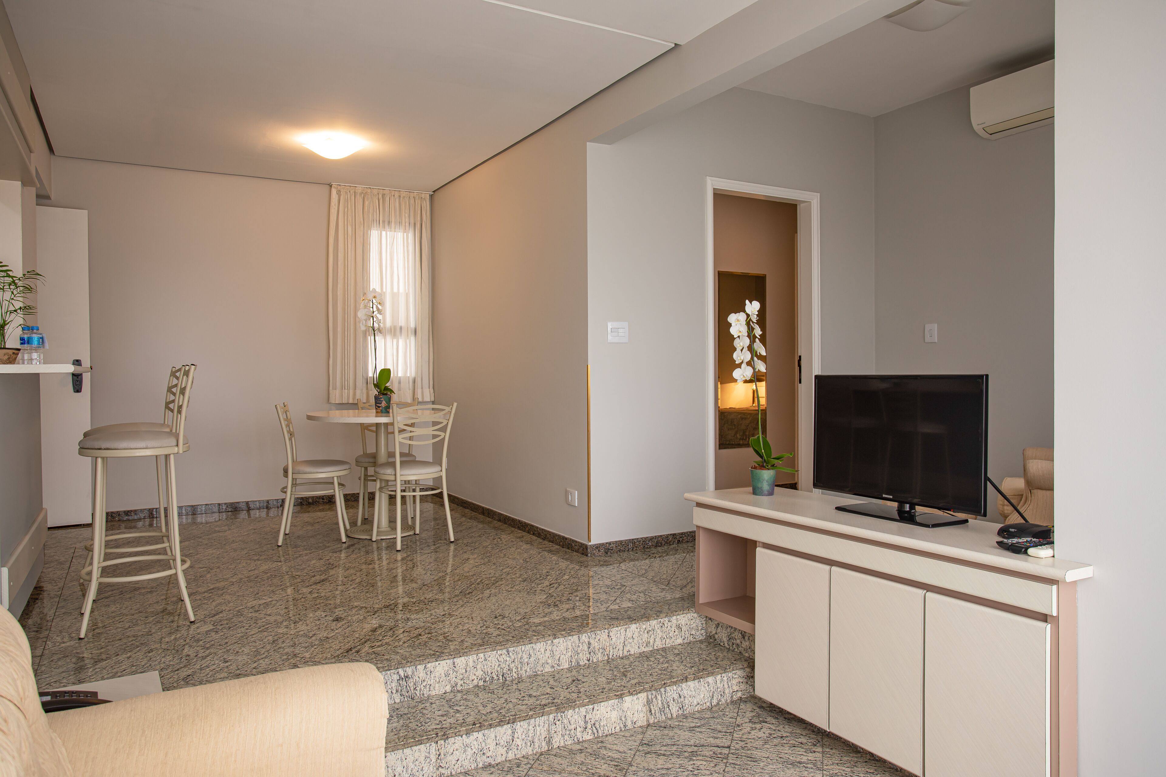 Un salon moderne doté d’un téléviseur à écran plat, d’un coin repas avec une table et des chaises, et d’un escalier menant à un autre niveau.
