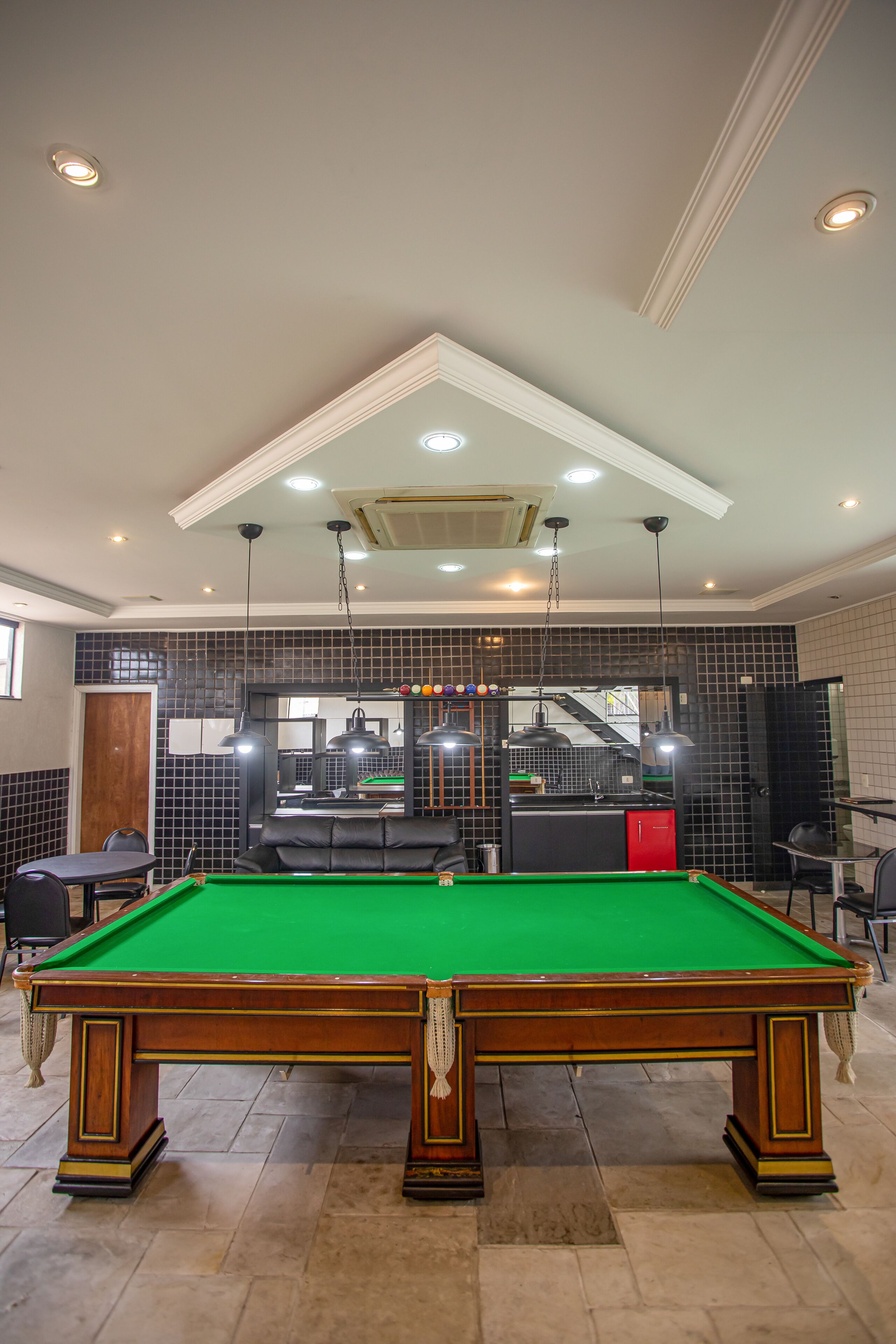 A pool table in a room with a tiled wall, a staircase, and a red cabinet.