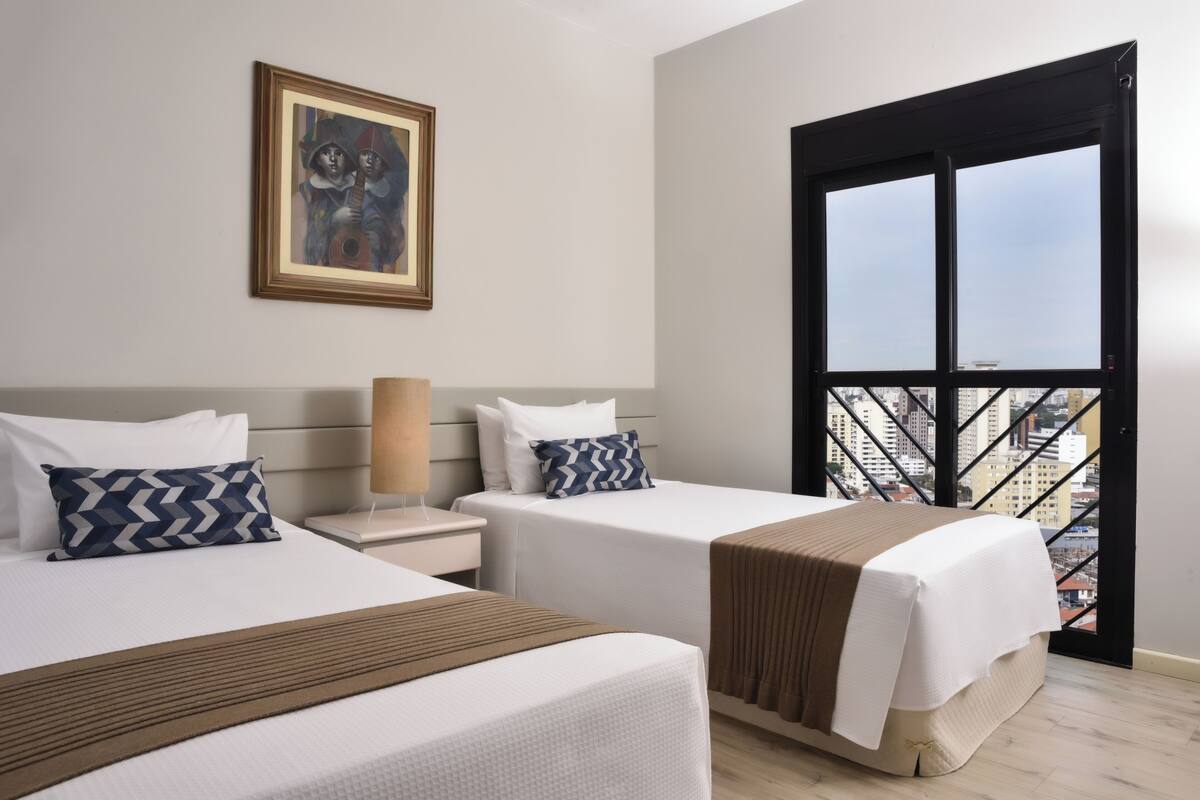 Habitación de hotel con dos camas, un cuadro enmarcado en la pared y un balcón con vistas a la ciudad.
