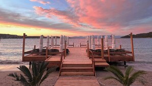 A wooden deck with lounge chairs and umbrellas, overlooking a calm body of water at sunset.